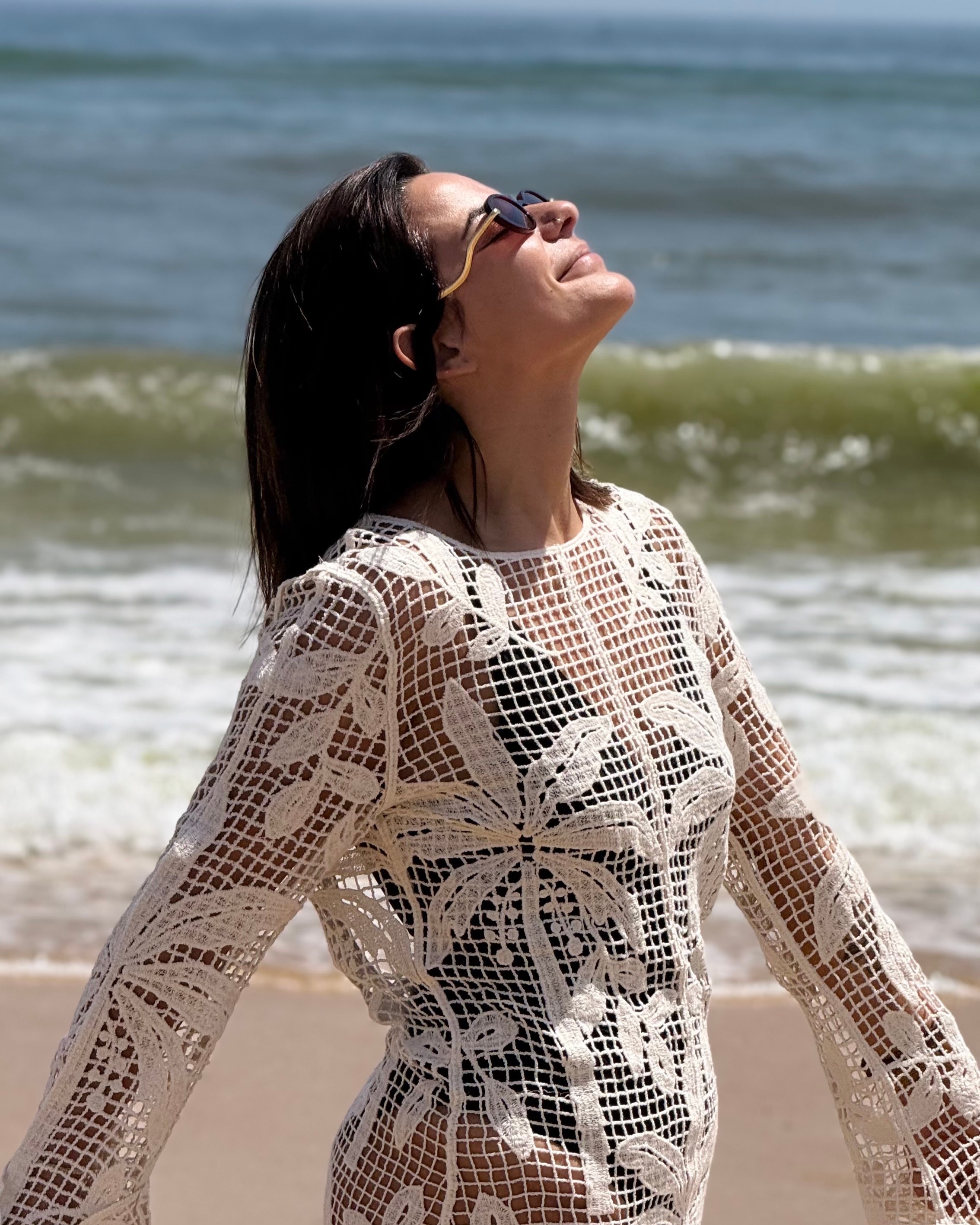 Joana with her face to the sun on a beach, sea behind her